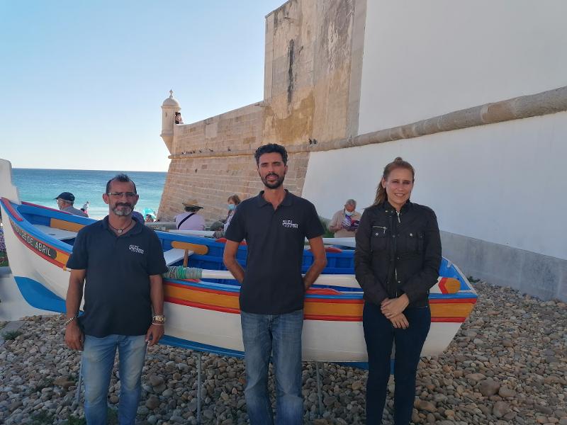 Three persons in front of a local fishing boat, an aiola, in Sesimbra. 